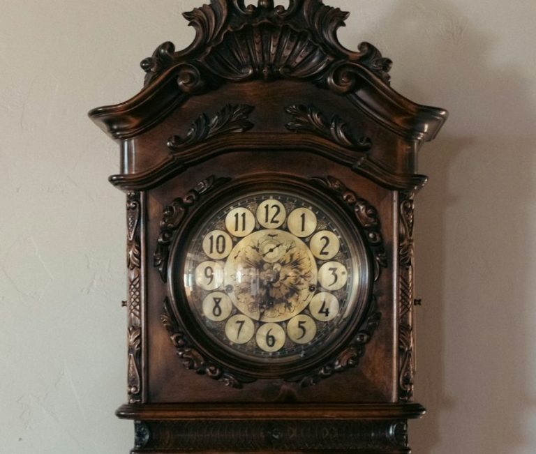 Antike Wanduhr aus dunklem Holz mit verziertem Gehäuse.