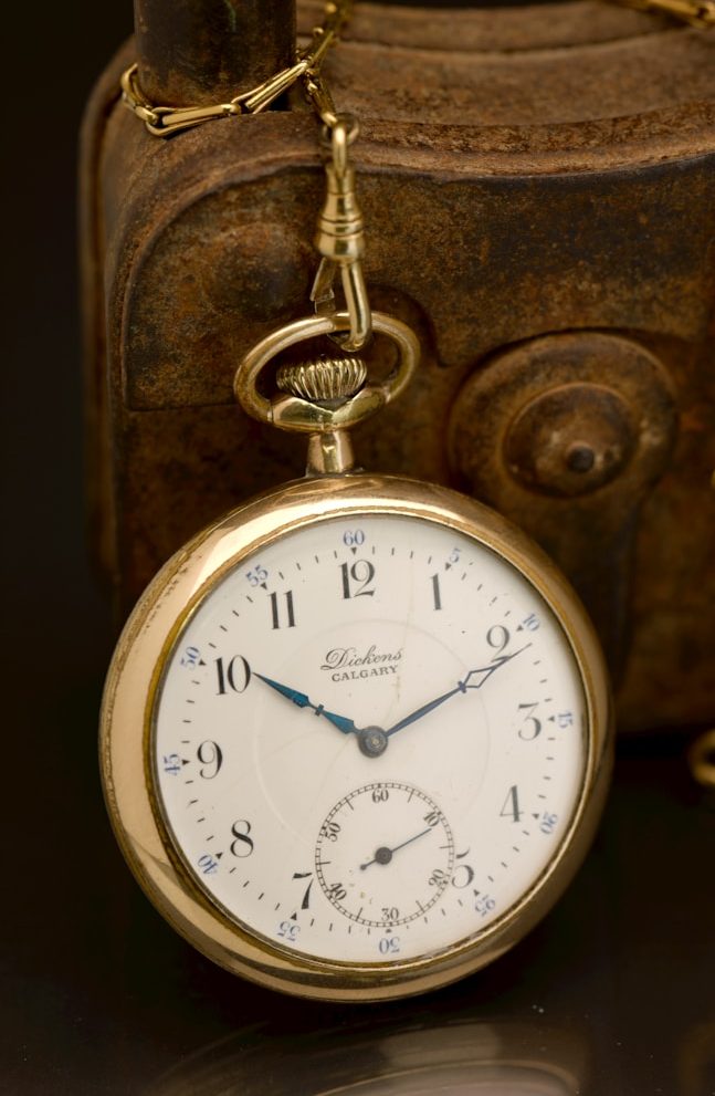 Eine goldene Taschenuhr mit einem weißen Zifferblatt und blauen Zeigern.